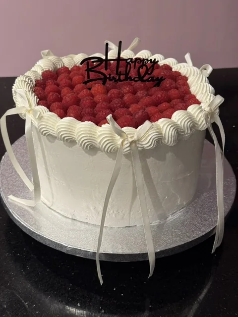 Layer cake blanc garni de framboises, nœuds ivoire et topper Happy Birthday