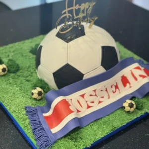Gâteau en forme de ballon de foot sur pelouse, écharpe de supporter